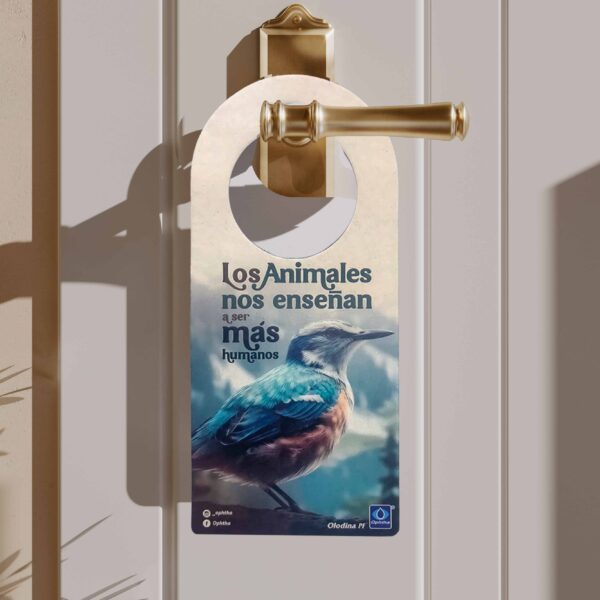 Colgapuertas ecológico colgado en una manija dorada, con ilustración de un ave colorida y la frase “Los animales nos enseñan a ser más humanos”. Producto de la línea ecológica ideal como regalo corporativo con mensaje de conciencia ambiental.