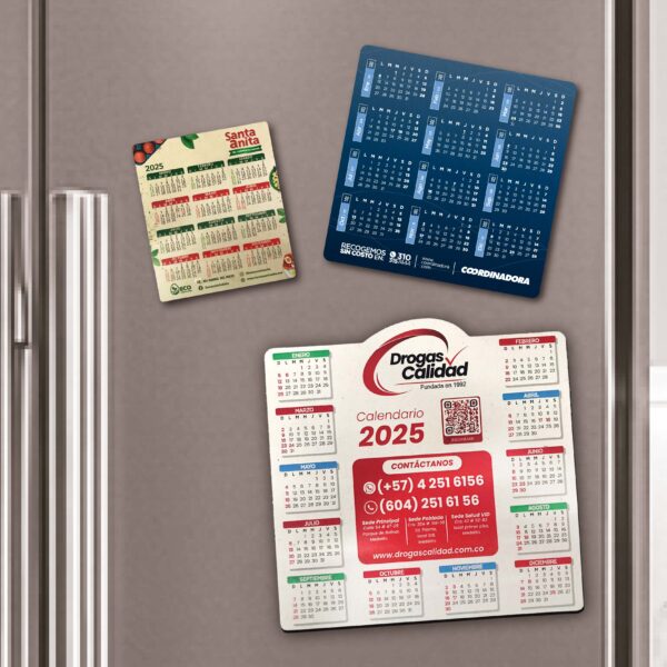 Tres calendarios magnéticos del año 2025 adheridos a una nevera. Uno de ellos con diseño ecológico de la marca Santa Anita, otro de color azul de Coordinadora, y un tercero de Drogas Calidad con información de contacto. Producto de la subcategoría Línea Ecológica ideal para regalar y mantener presencia de marca todo el año.