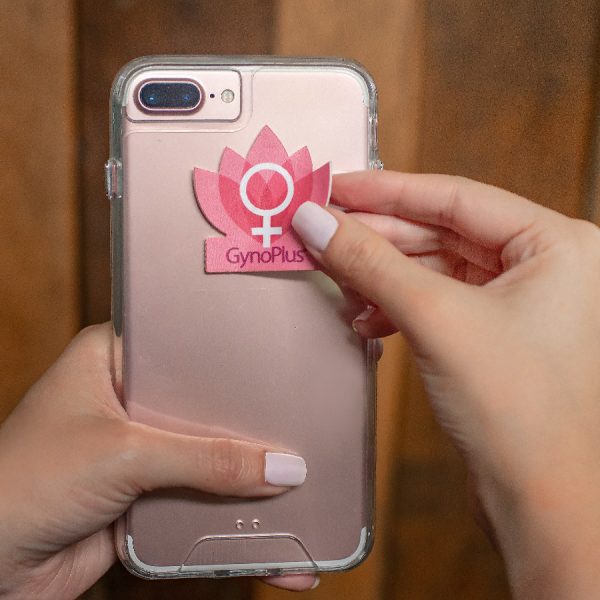 Sticker limpiador promocional GynoPlus con diseño corporativo adherido a la parte trasera de un celular.